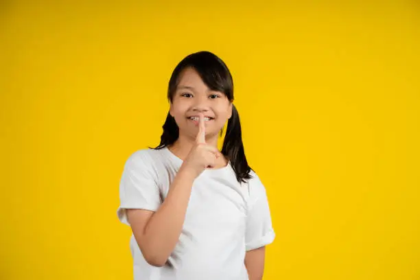 Keep Silence Concept. Cheerful asian child puting finger on lips.