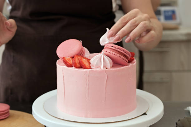 istock Woman pastry chef decorates pink cake with macaroons and berries, close-up. Cake making process, Selective focus 1334960499