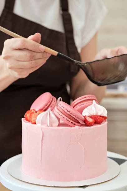 istock Woman pastry chef decorates pink cake with macaroons and berries, close-up. Cake making process, Selective focus 1334960504