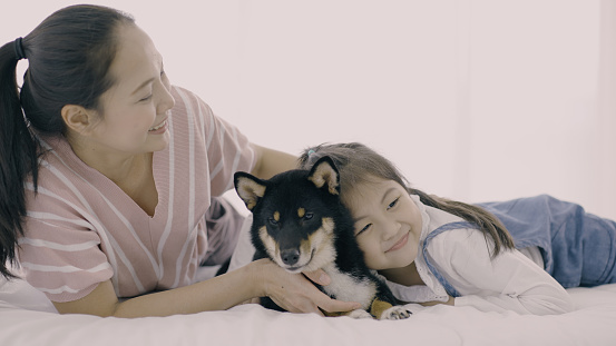 Happy daughter and mother loving their cute black dog on bed.