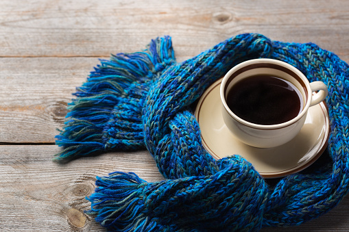 Autumn, fall, winter home decor in scandinavian, hygge style. Seasonal composition with cup of coffee, warm woolen scarf, soft plaid on a rustic wooden table.