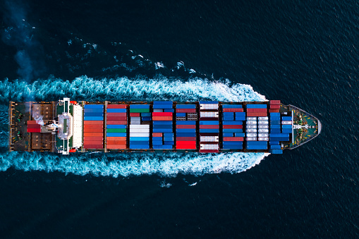 container ship full speed transporting large cargo logistic import export goods internationally worldwide including Asia Pacific and Europe, industry business service transportation by container ship in dark sea or Mediterranean photograph aerial top view from drone,