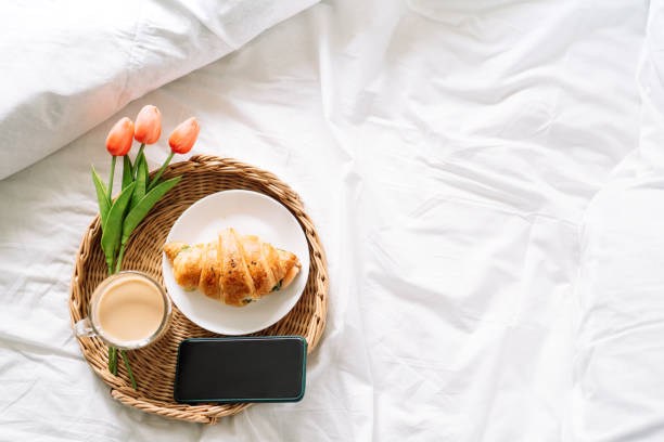 istock Croissant and coffee on white bed on wicker tray with flowers 1334976549