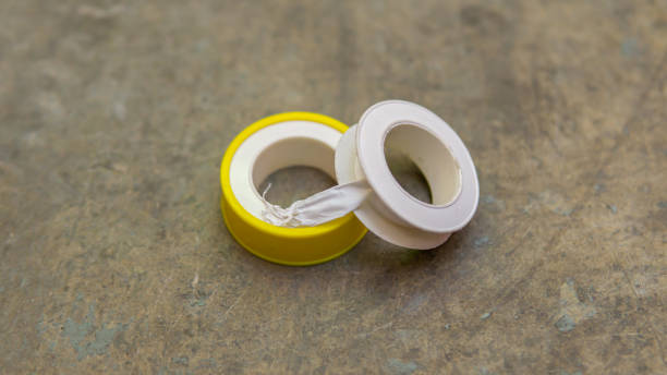 White tape or thread seal tape with yellow casing on the floor. White tape or thread seal tape with yellow casing on the floor. It is a polytetrafluoroethylene (PTFE) film tape commonly used in plumbing for sealing pipe threads. Selective focus on object. polytetrafluoroethylene photos stock pictures, royalty-free photos & images