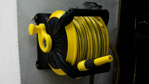 A yellow wall mounted garden water hose reel with sprinkler or sprayer. Cleaning tool, garden and utility in home concept.