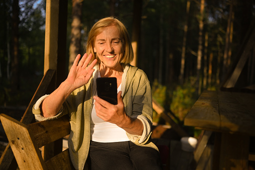 attractive happy senior elderly woman having video chat outdoors waving conversation on