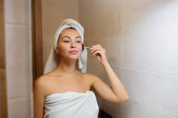 spa i kosmetologia. pielęgnacja skóry twarzy w domu. dziewczyna w łazience nakłada kremową maskę na twarz - clear sky human skin towel spa treatment zdjęcia i obrazy z banku zdjęć