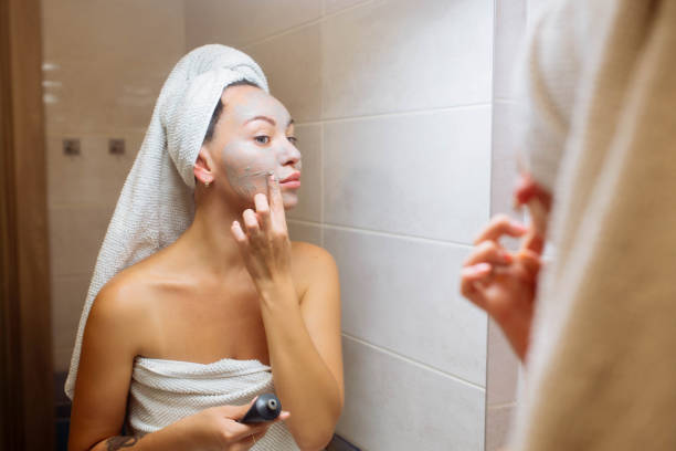 spa i kosmetologia. pielęgnacja skóry twarzy w domu. dziewczyna w łazience nakłada kremową maskę na twarz - clear sky human skin towel spa treatment zdjęcia i obrazy z banku zdjęć