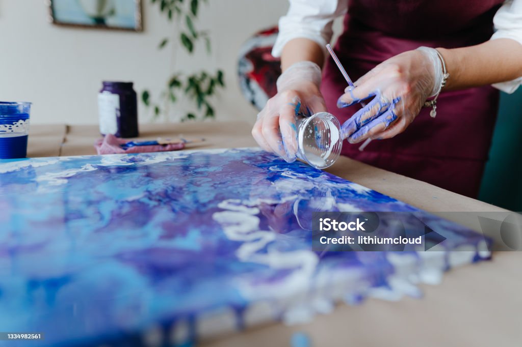 Artist mixing acryl paints on the picture working in fluid art technique Female artist mixing acryl paints on the picture working in fluid art technique. Selective focus. Pouring Stock Photo