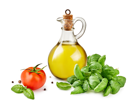 Glass jar of olive or vegetable oil with basil leaves and tomato isolated on white.