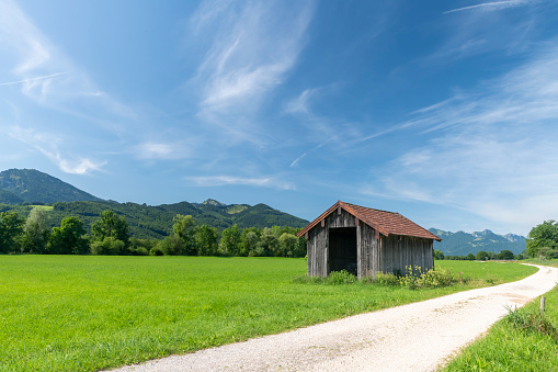 Bavarian meadow landscape with wooden hut, light path, blue sky and copy space