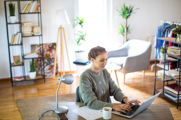 istock Young woman sitting at desk and working from home using laptop 1334985352
