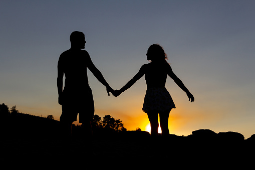 Loving couple holding hands in a romantic sunset on a lake. Backlight. Copy space. Autumn.
