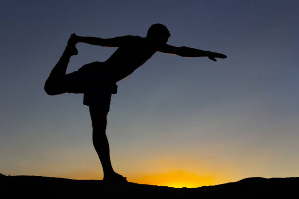istock Silhouette of man practicing yoga at sunset on a rock in nature. Backlight. Copy space. 1334985568