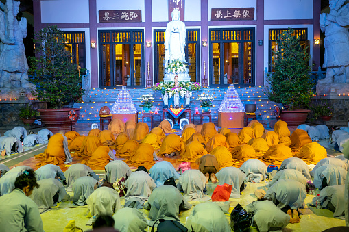 Ho Chi Minh City, Vietnam - December 12th, 2019: Monks and Buddhists are reverently bowing to Buddha during evening ceremony for Amitabha Buddha at an ancient temple in Ho Chi Minh City, Vietnam