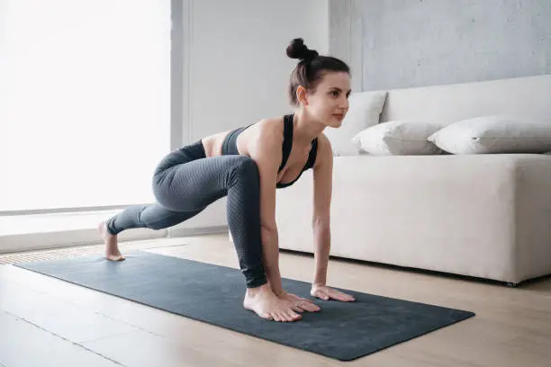 Concentrated young woman performing lizard exercise with straight arms position during her morning yoga practice at home. Healthy lifestyle, fitness and body strength development