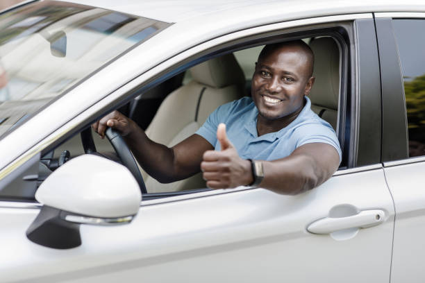 istock Happy black man driving luxury white car, showing thumb up 1334994534