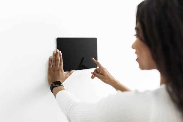 istock Young black lady controlling house with digital touch screen panel installed on white wall in the living room, mockup 1334994592