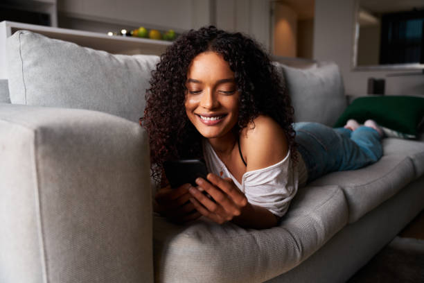 istock Mixed race female student relaxing on couch texting on cellular device 1334994674