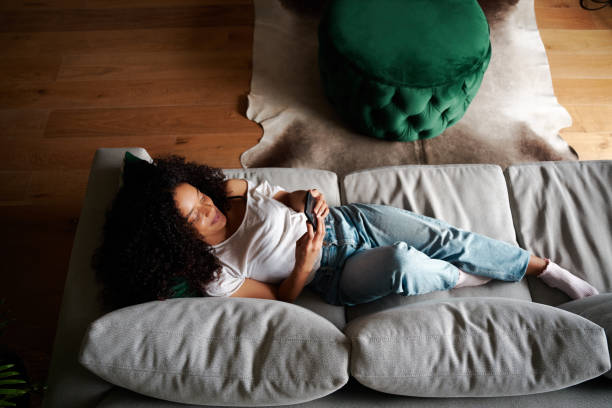 istock Mixed race female student relaxing on couch texting on cellular device 1334994719
