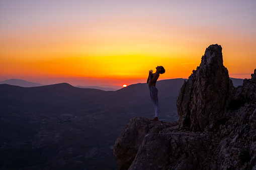 Woman practices yoga and meditating on the mountain sunset.