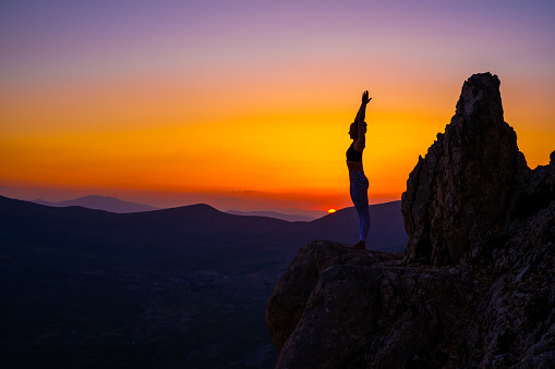 Woman practices yoga and meditating on the mountain sunset.