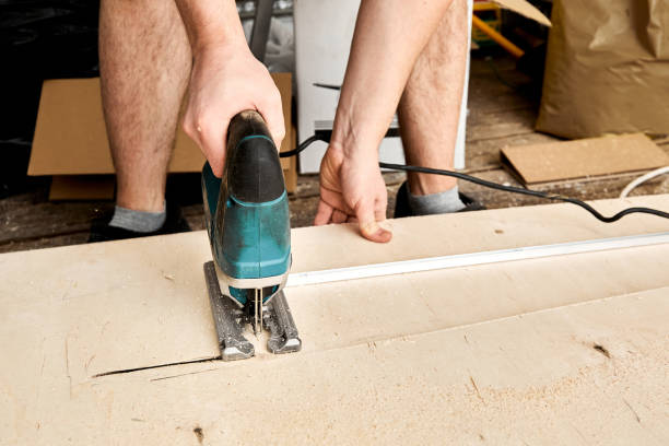 Male hands of construction worker sawing and cutting parts with an electric jigsaw from plywood. The cut process. DIY building of interior decoration with fretsaw. Rental tool. Copy space. Equipment. manos masculinas de trabajadores de la construcción que aserrban y cortan piezas con un rompecabezas eléctrico de madera contrachapada. el proceso de corte. edificio de bricolaje de decoración de interiores con trastes. herramienta de alquiler. espacio