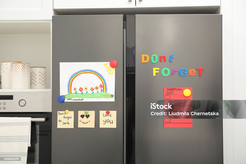 Modern refrigerator with child's drawing, notes and magnets in kitchen Refrigerator Stock Photo