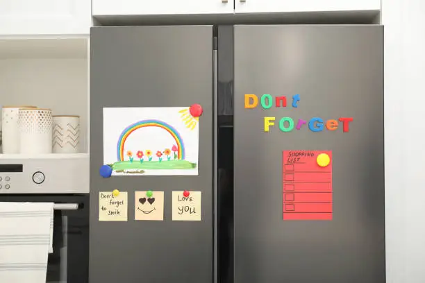Photo of Modern refrigerator with child's drawing, notes and magnets in kitchen