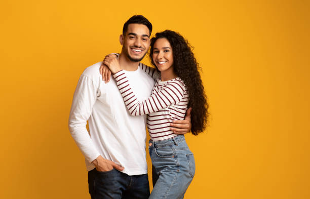 Portrait of joyful romantic middle-eastern couple embracing while posing over yellow background Portrait of joyful romantic middle eastern couple embracing each other while posing over yellow studio background, young happy arab man and woman hugging and smiling at camera, copy space middle eastern ethnicity photos stock pictures, royalty-free photos & images