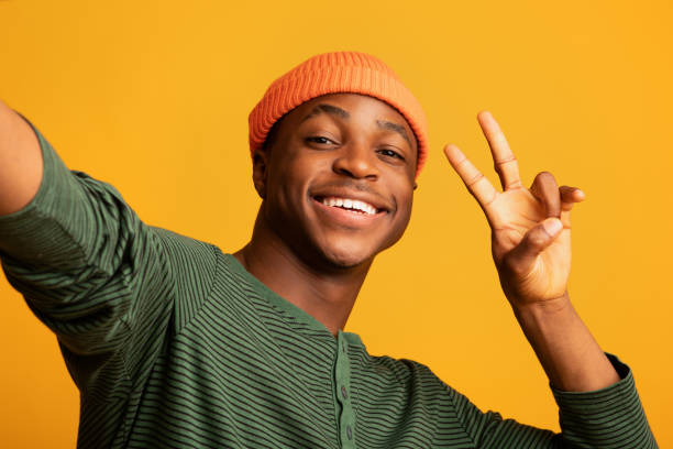 istock Cheerful Black Hipster Guy In Orange Hat Taking Selfie, Showing Peace Gesture 1335002557