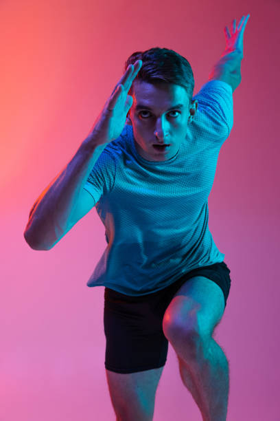 istock Close up Caucasian professional male athlete, runner training isolated on pink studio background with blue neon filter, light. Muscular, sportive man. 1335003088
