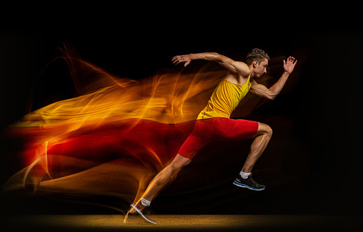 Portrait of young man, professional male athlete, runner in motion and action isolated on dark background. Stroboscope effect. Concept of healthy lifestyle, sport, action, achievemnts, goal, ad.