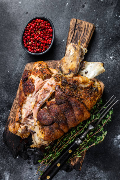 istock Roasted pork knuckle eisbein on a wooden board with herbs. Black background. Top view 1335007610