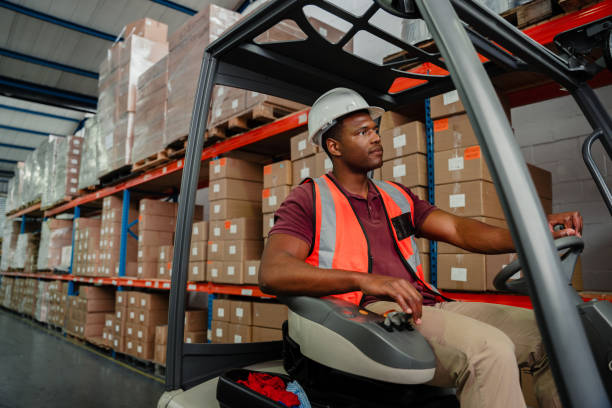 istock Ethnic worker driving in forklift around warehouse searching for packages to send off delivery 1335008506