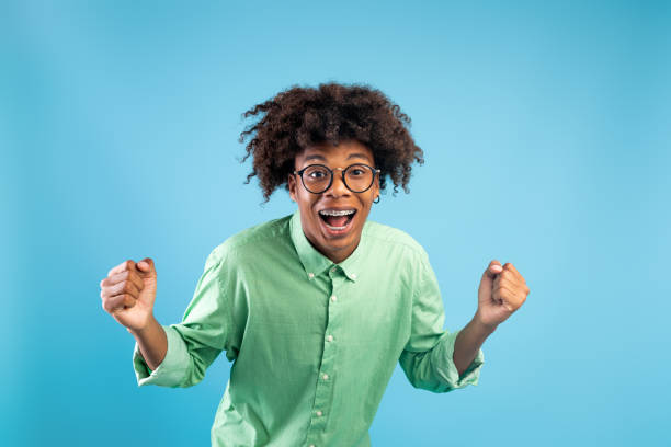 istock Yeah, I did it. Overjoyed african-american guy shaking clenched fists, charing and rejoicing success, blue background 1335009539