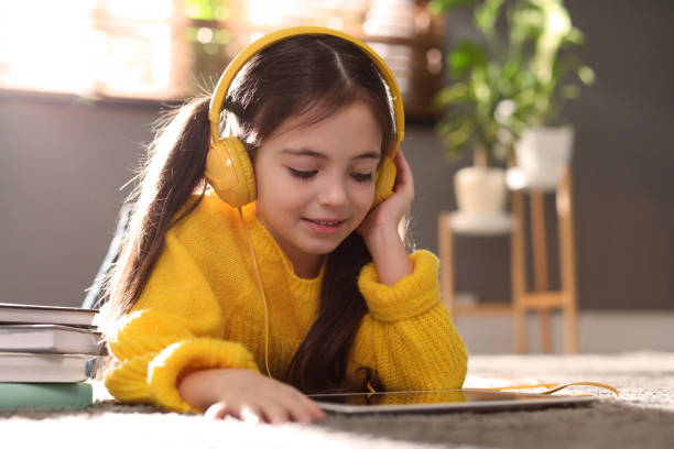 Cute little girl with headphones and tablet listening to audiobook at home Cute little girl with headphones and tablet listening to audiobook at home audio book stock pictures, royalty-free photos & images