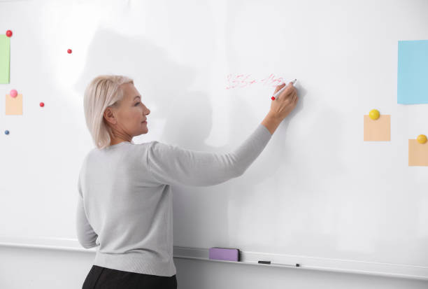 istock Mature teacher writing on whiteboard in classroom 1335009975