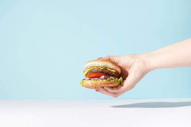 mano sosteniendo una hamburguesa sobre fondo azul. alimentación y concepto saludable, espacio de copia - roll of arms fotografías e imágenes de stock