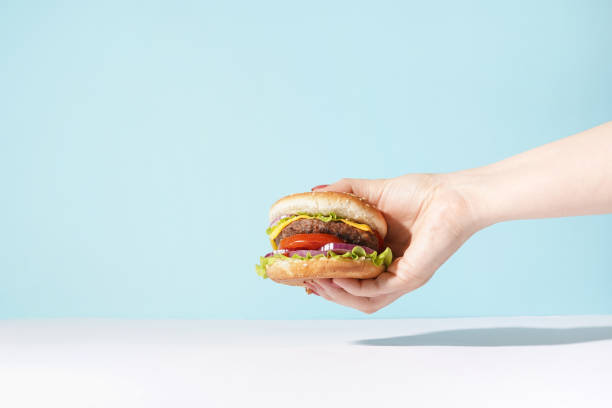 istock Hand holding a burger on blue background. eating and healthy concept, copy space 1335017510