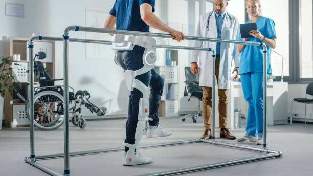 istock Modern Hospital Physical Therapy: Patient with Injury Walks Wearing Advanced Robotic Exoskeleton. Physiotherapy Rehabilitation Scientists, Engineers use Tablet Computer to Help Disabled Person 1335020207