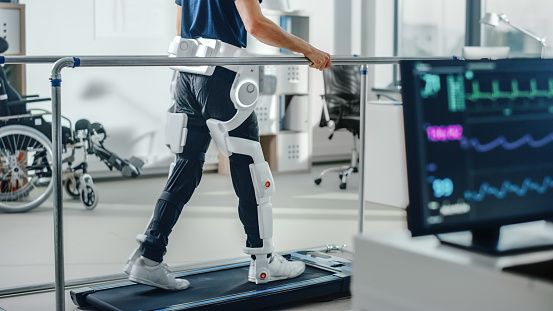 Terapia física moderna del hospital: El paciente con lesión camina en la cinta de correr usando las piernas robóticas avanzadas del exoesqueleto. Tecnología de rehabilitación de fisioterapia para hacer caminar a las personas discapacitadas. Concéntre photo