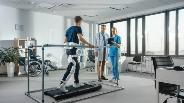 Modern Hospital Physical Therapy: Patient with Injury Walks on Treadmill Wearing Advanced Robotic Exoskeleton. Physiotherapy Rehabilitation Scientists, Engineers, Doctors use Tablet Computer to Help Modern Hospital Physical Therapy: Patient with Injury Walks on Treadmill Wearing Advanced Robotic Exoskeleton. Physiotherapy Rehabilitation Scientists, Engineers, Doctors use Tablet Computer to Help powered exoskeleton photos stock pictures, royalty-free photos & images