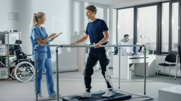 Modern Hospital Physical Therapy: Doctor Uses Tablet Computer, Helps Disabled Patient with Injury Walk on Treadmill Wearing Advanced Robotic Exoskeleton Legs. Physiotherapy Rehabilitation Technology Modern Hospital Physical Therapy: Doctor Uses Tablet Computer, Helps Disabled Patient with Injury Walk on Treadmill Wearing Advanced Robotic Exoskeleton Legs. Physiotherapy Rehabilitation Technology powered exoskeleton photos stock pictures, royalty-free photos & images