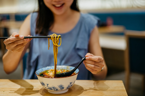 Image of a smiling young woman enjoying a bowl of noodle soup in chinese restaurant