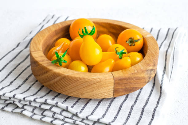 Small yellow tomatoes in wooden bowl on white background. Closeup image of yellow pear tomatoes. Organic healthy food. stock photo