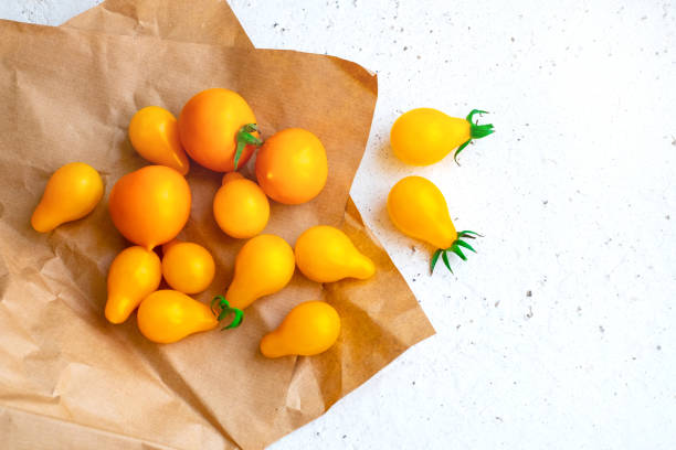 Small yellow tomatoes on craft paper on white background. Closeup image of yellow pear tomatoes. Organic healthy food. stock photo