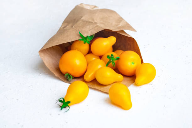 Small yellow tomatoes spilled out of craft paper bag on white background. Closeup image of yellow pear tomatoes. Organic healthy food. stock photo