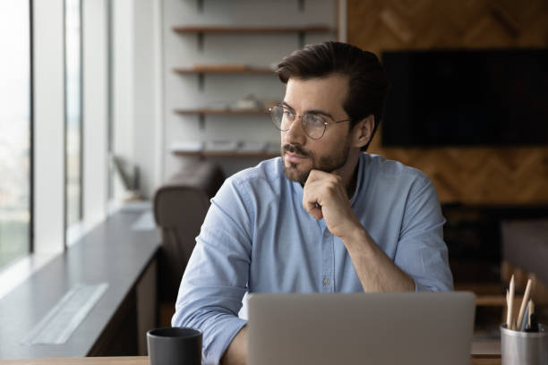 Thoughtful businessman in glasses looking at window from workplace