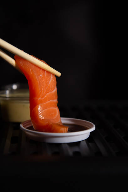 lachs sashimi im japanischen buffet-restaurant-menü. die hände hielten die essstäbchen, um das frische lachs-sashimi mit sojasauce mit kopierraum zu halten. - sashimi stock-fotos und bilder